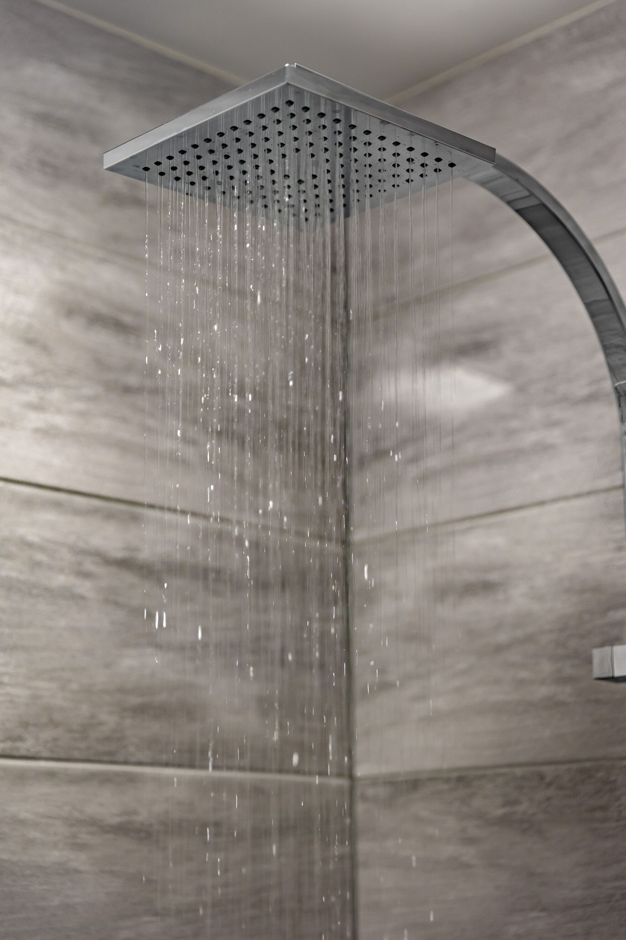 Une pomme de douche moderne au design incurvé, laissant jaillir l’eau, avec un mur en marbre en arrière-plan.
