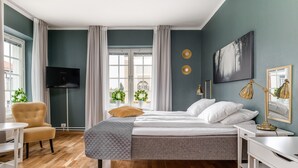 A modern bedroom with a bed, a desk, a chair, a TV, and a window with curtains. - Ludvika Stadshotell (Ludvika)