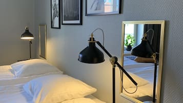 A neatly made bed with white linens, a bedside table with a lamp, and a wall with framed pictures.