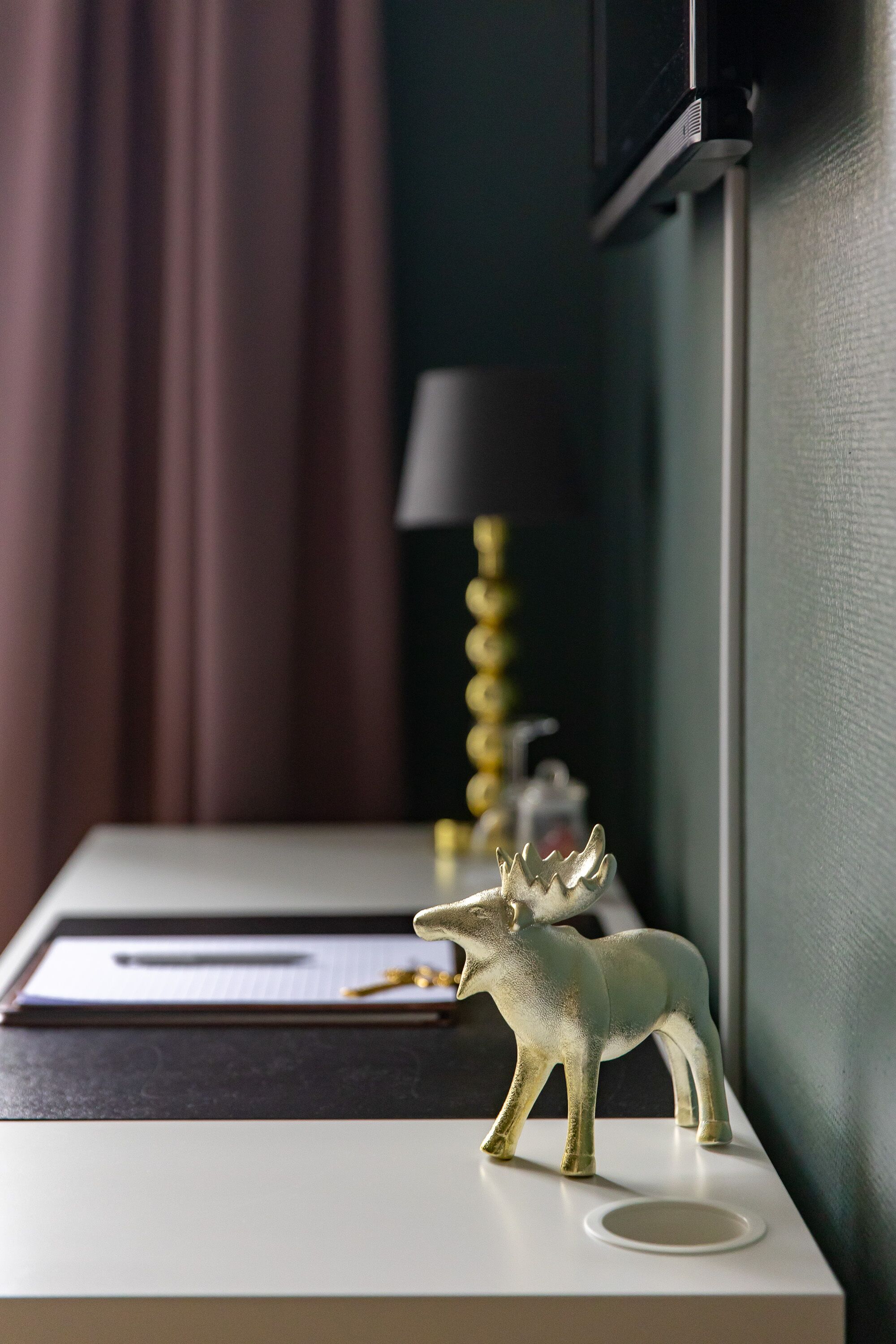 A desk with a moose figurine, a lamp, and a pen on a notepad.