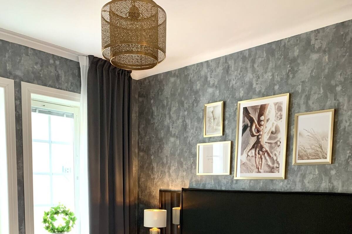 Une chambre moderne avec un grand lit, une tête de lit sombre et une vue sur l’extérieur par une fenêtre.