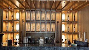 A bar area with wooden shelves displaying bottles, a marble countertop, and bar stools. - The Manor - New Delhi (New Delhi)