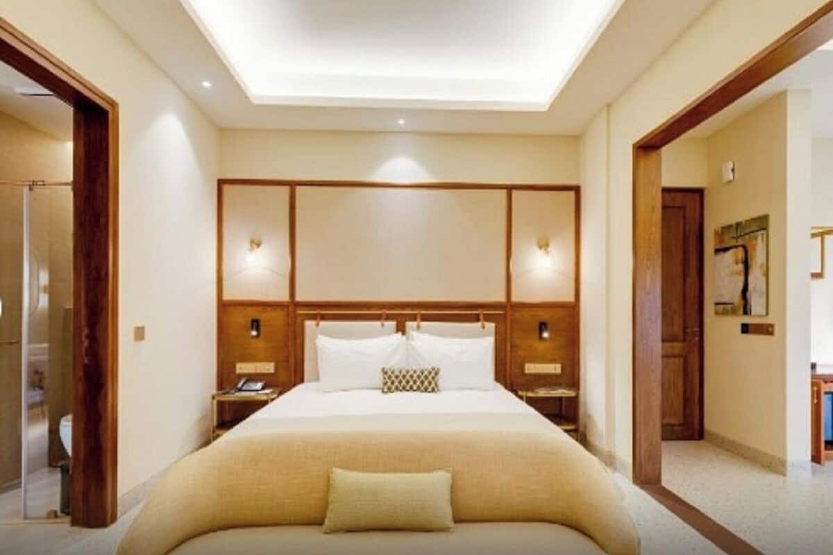 A hotel room with a large bed, wooden headboard, bedside lamps, and a view of the hallway.