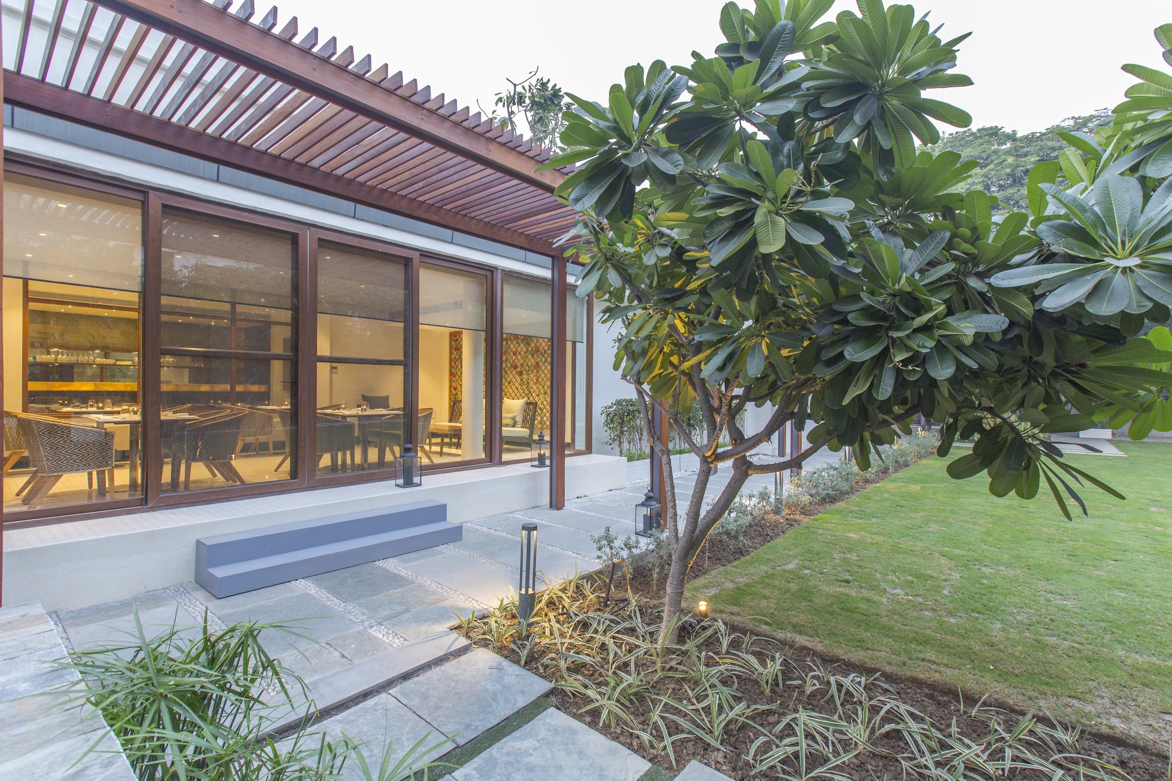 A modern house with large glass windows, a wooden pergola, and a well-maintained garden.