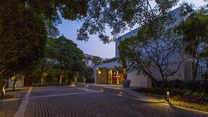 A modern building with a paved entrance, surrounded by trees and greenery. - The Manor - New Delhi (New Delhi)