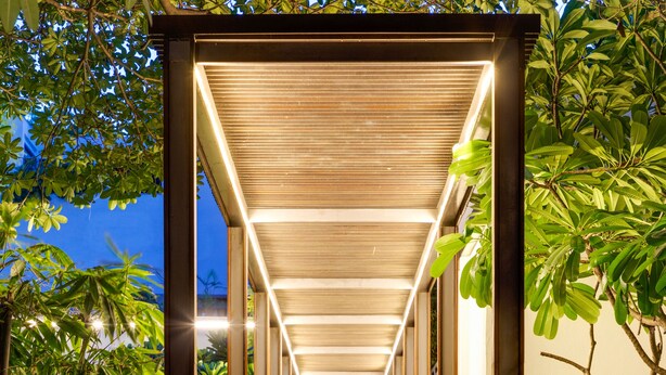 A covered walkway with a wooden door at the end, flanked by greenery and lanterns. - The Manor - New Delhi (New Delhi)