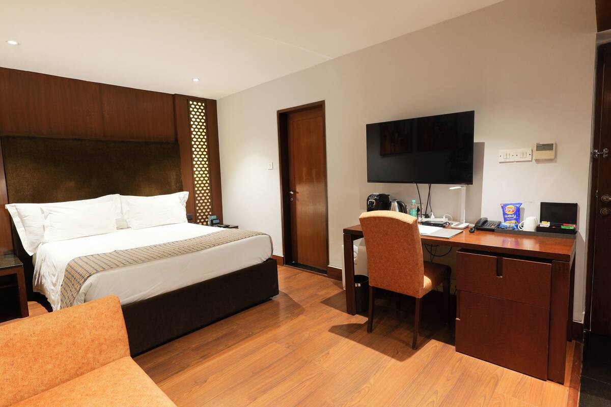 A hotel room with a bed, a desk with a chair, a television, and a small cabinet.