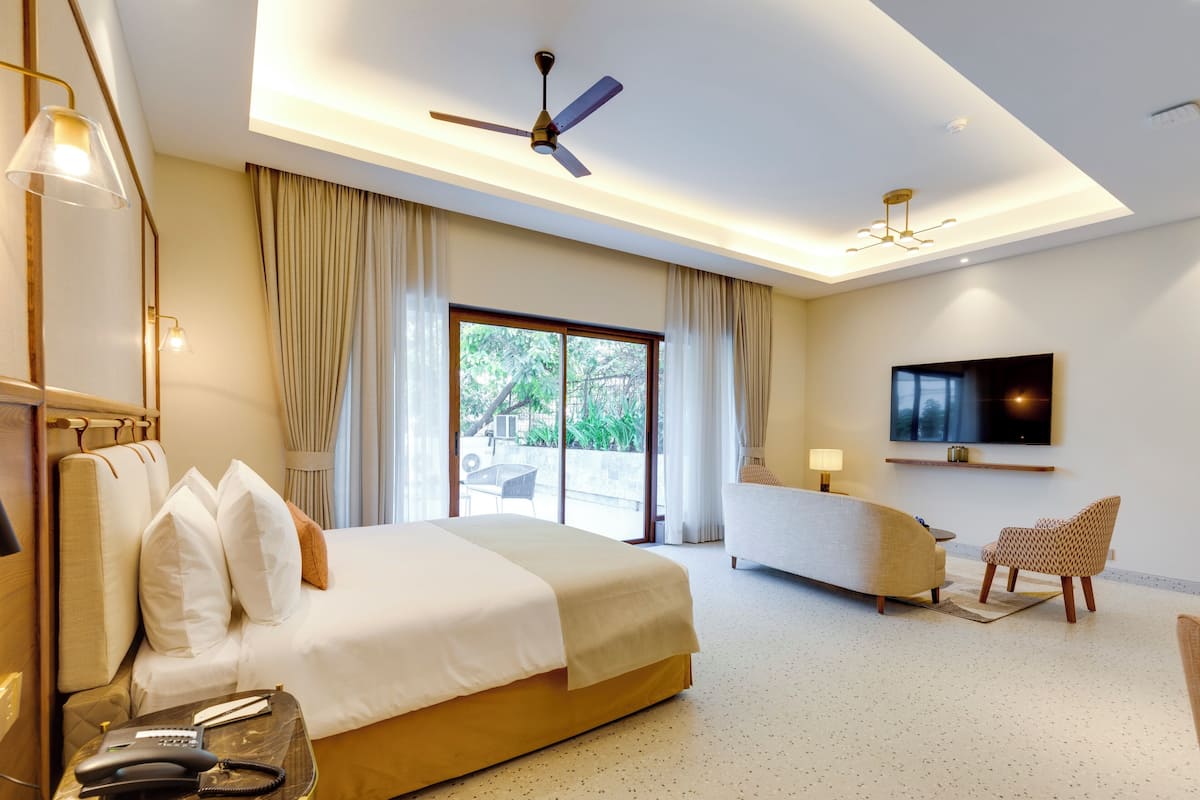 A hotel room with a large bed, a sofa, a TV mounted on the wall, and a ceiling fan.