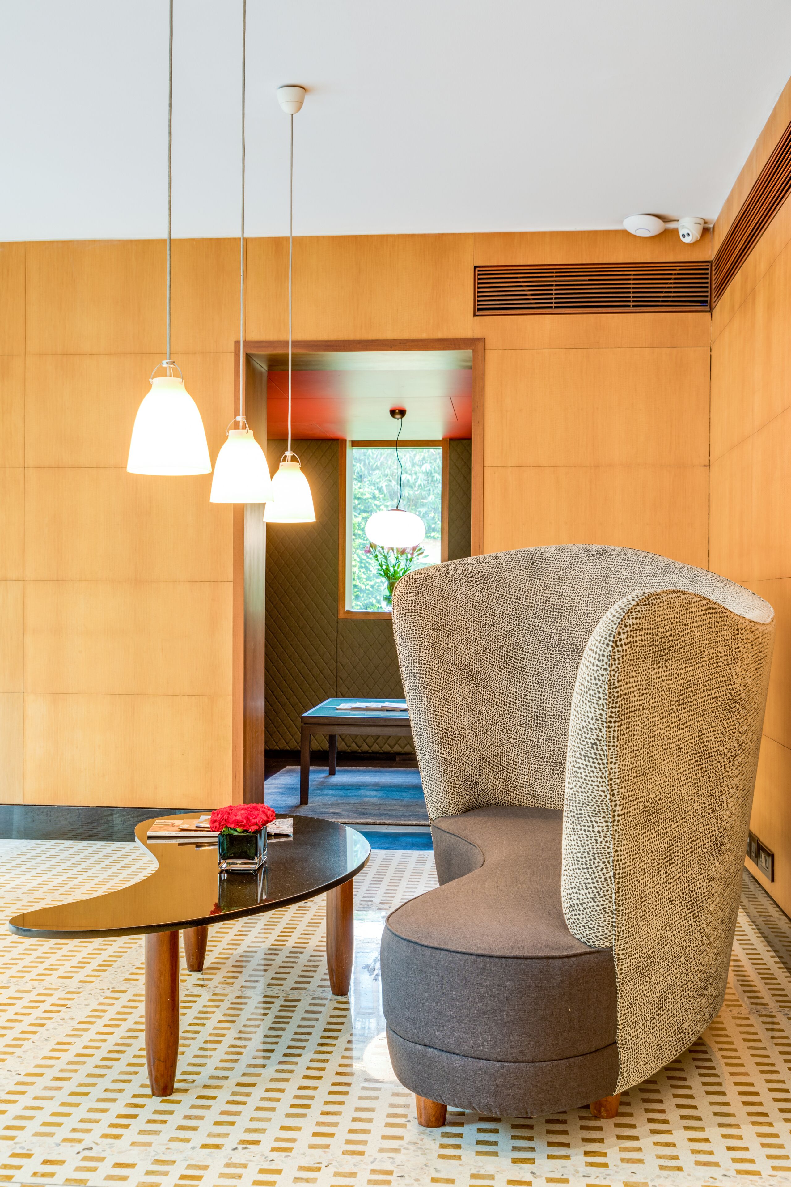 A modern interior with a round table, two pendant lights, a textured armchair, and a patterned floor.