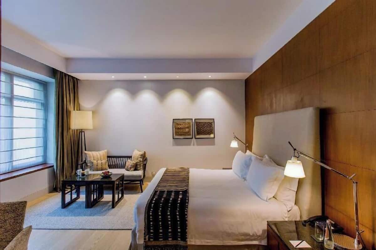 A hotel room with a bed, bedside table, lamp, and a view of the outside.