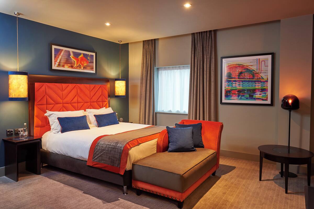 Une chambre d’hôtel moderne avec un grand lit, un canapé, une petite table et deux lampes fixées au mur.