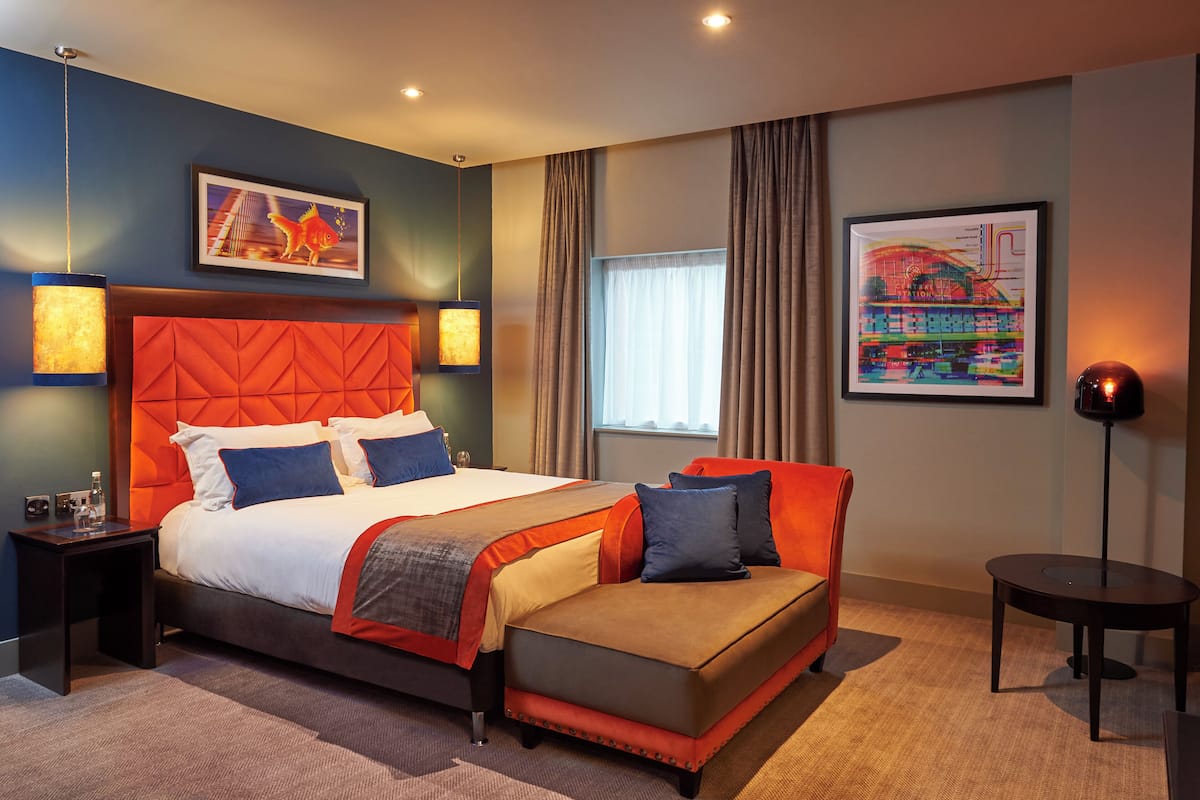 Une chambre d’hôtel moderne avec un grand lit, un canapé, une petite table et deux lampes fixées au mur.