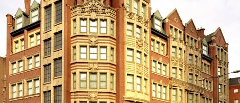 Un edificio grande e histórico con una entrada destacada en esquina, múltiples ventanas y una torre central.
