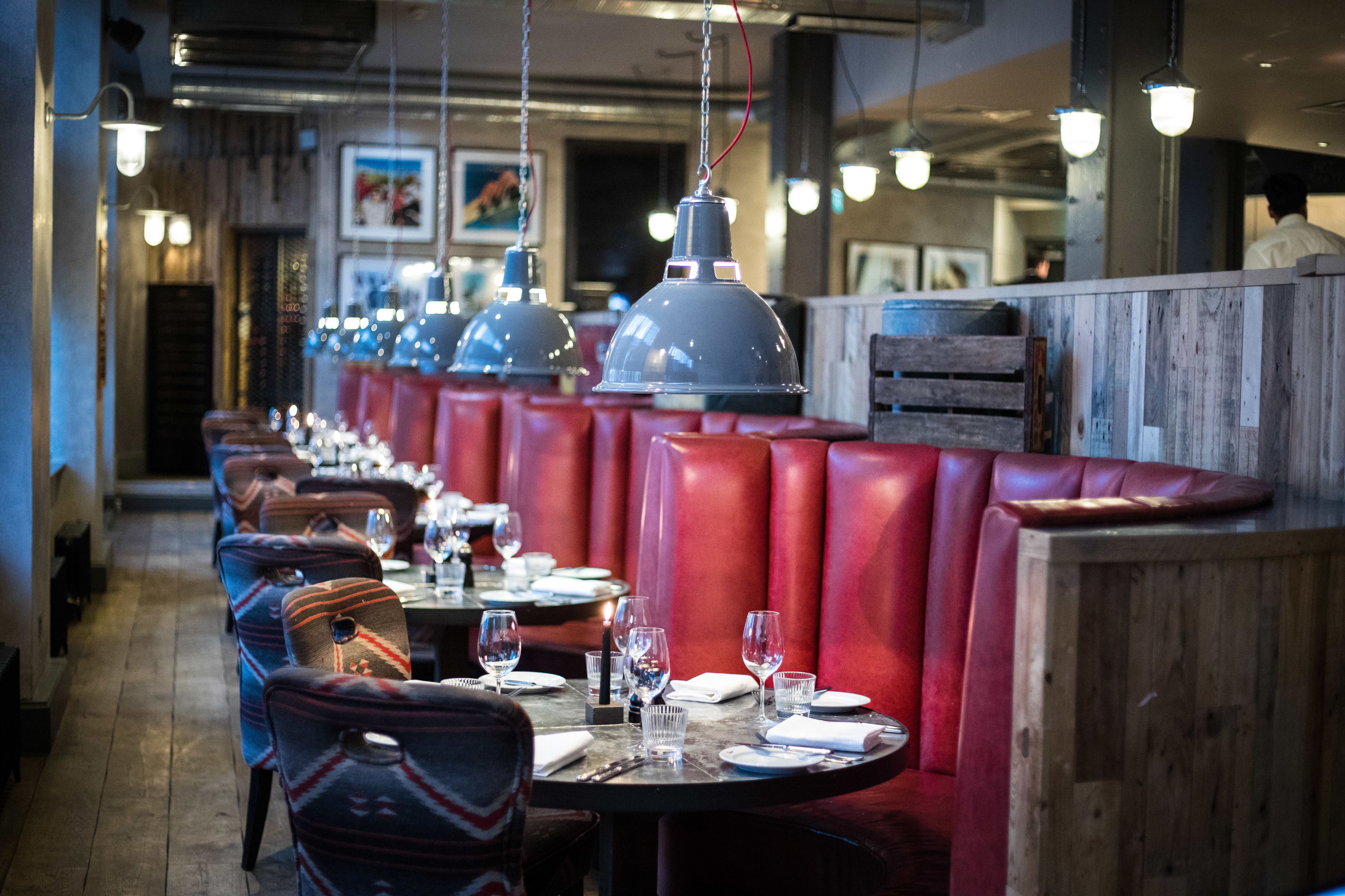 A restaurant interior with red booths, hanging pendant lights, and a long counter with tables set for dining.
