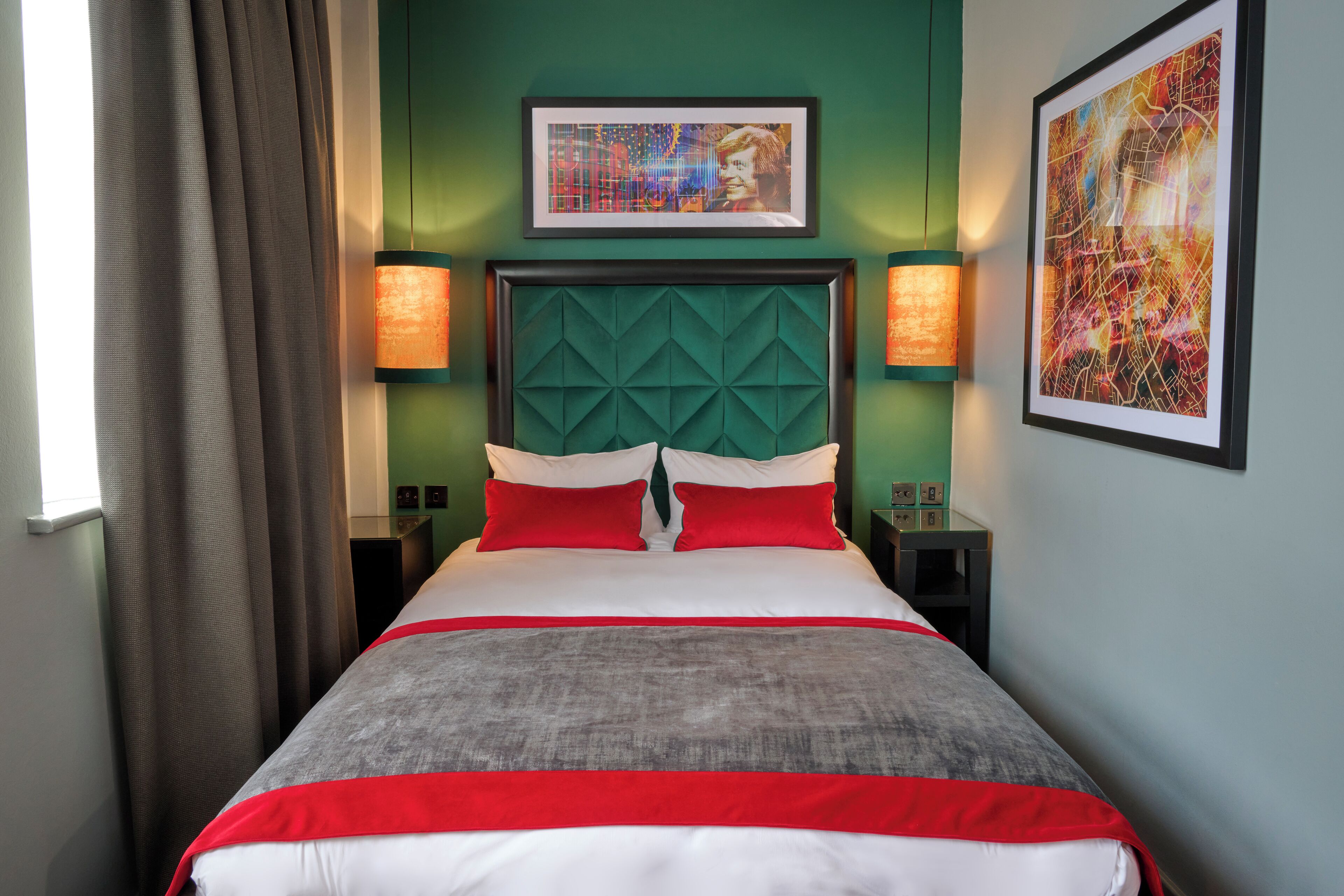 Quarto de hotel com uma cama grande, paredes verdes e duas mesas de cabeceira com luminárias.