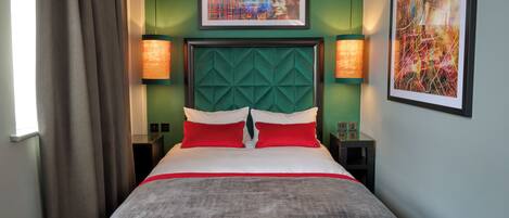 Quarto de hotel com uma cama grande, paredes verdes e duas mesas de cabeceira com luminárias.