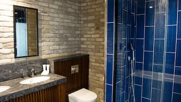 A bathroom with a stone wall, a wooden vanity, a white sink, and a blue-tiled shower area.