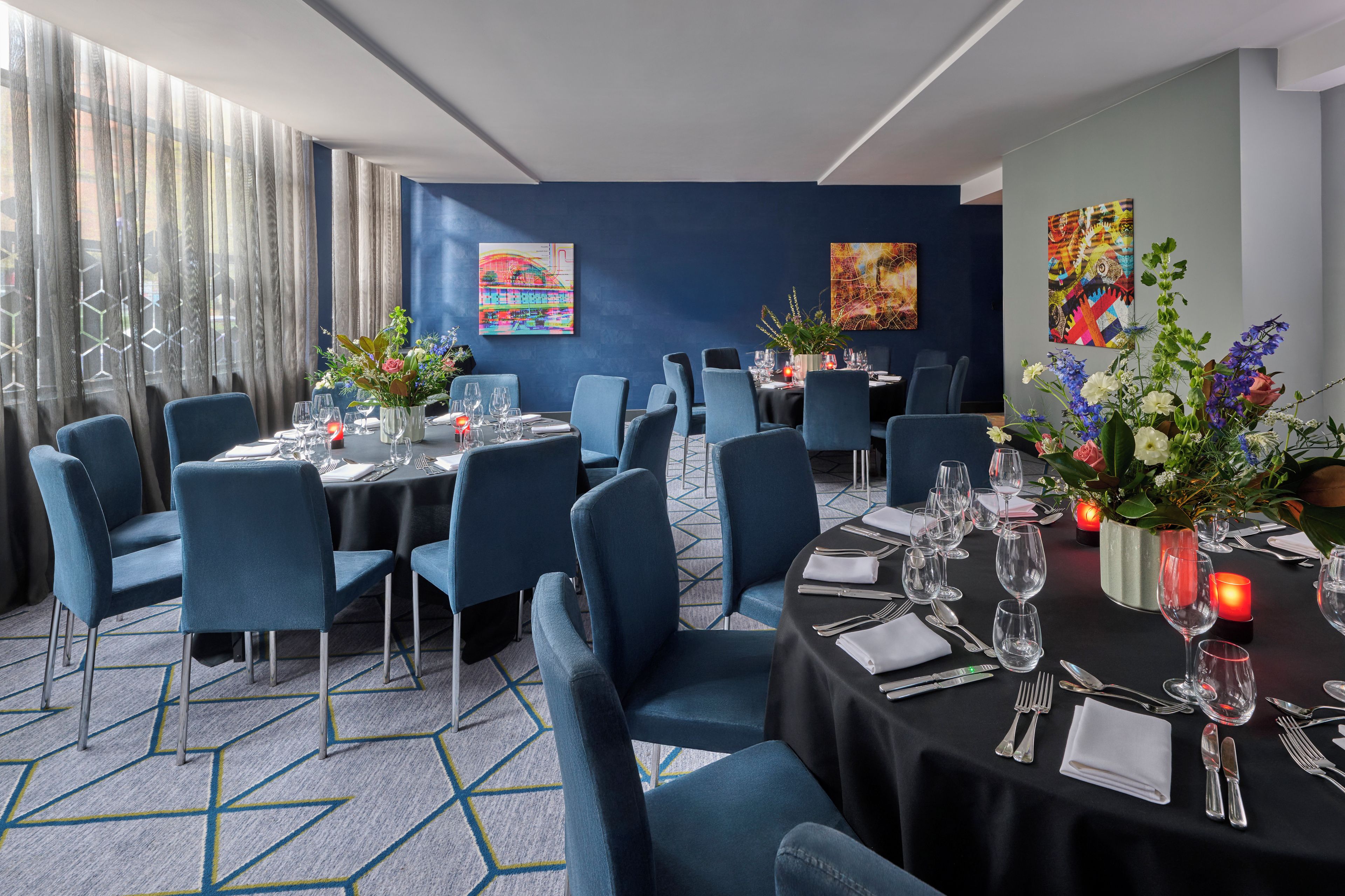 A dining area with tables set for six, blue chairs, and floral centerpieces.