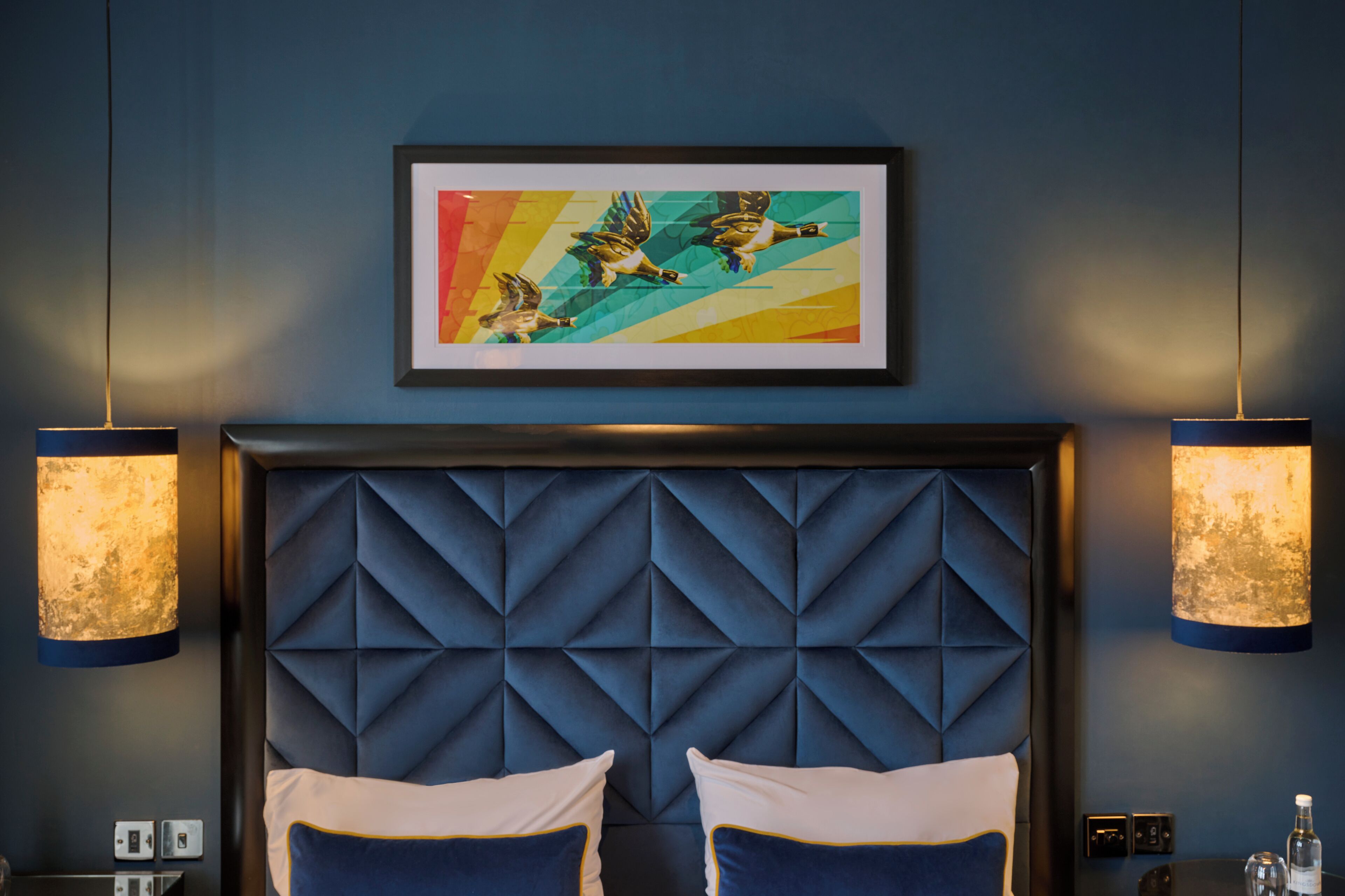 A hotel room with a tufted headboard, two bedside lamps, a framed artwork, and a bed with two pillows.