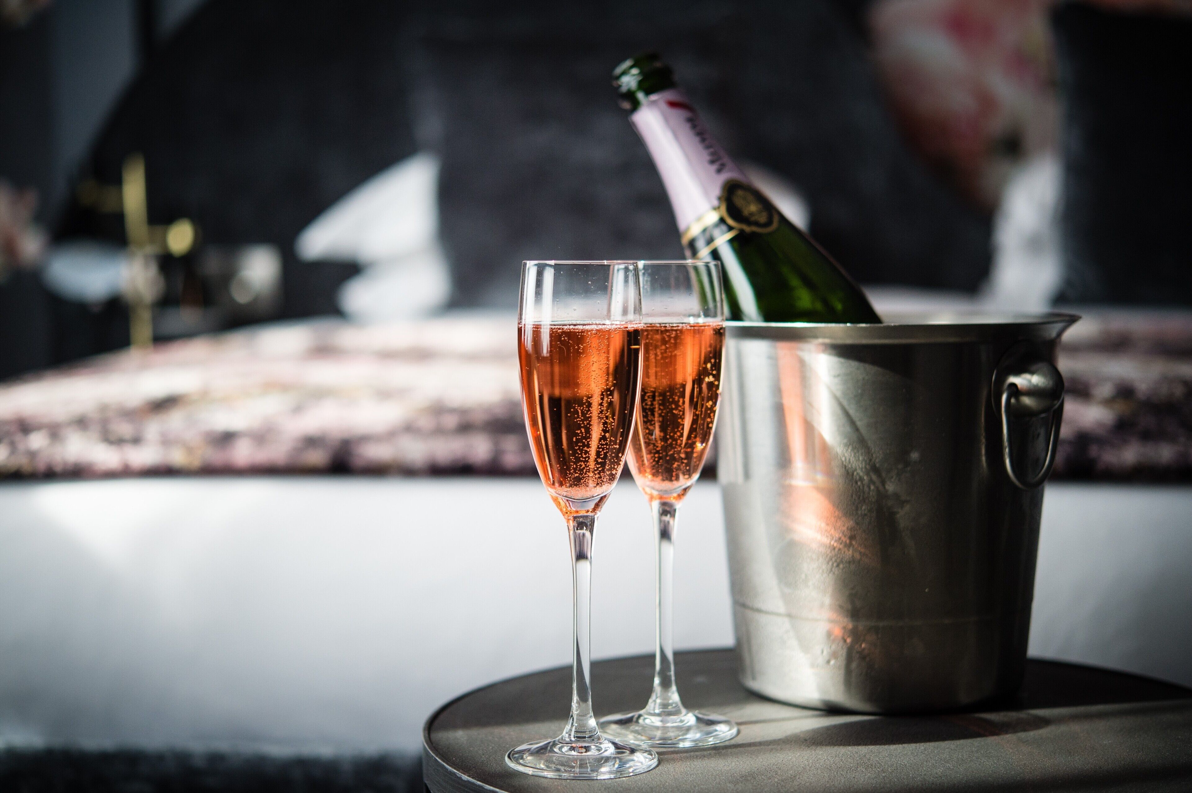 Two champagne flutes filled with a bubbly beverage, a bottle of champagne, and a metal bucket on a table.