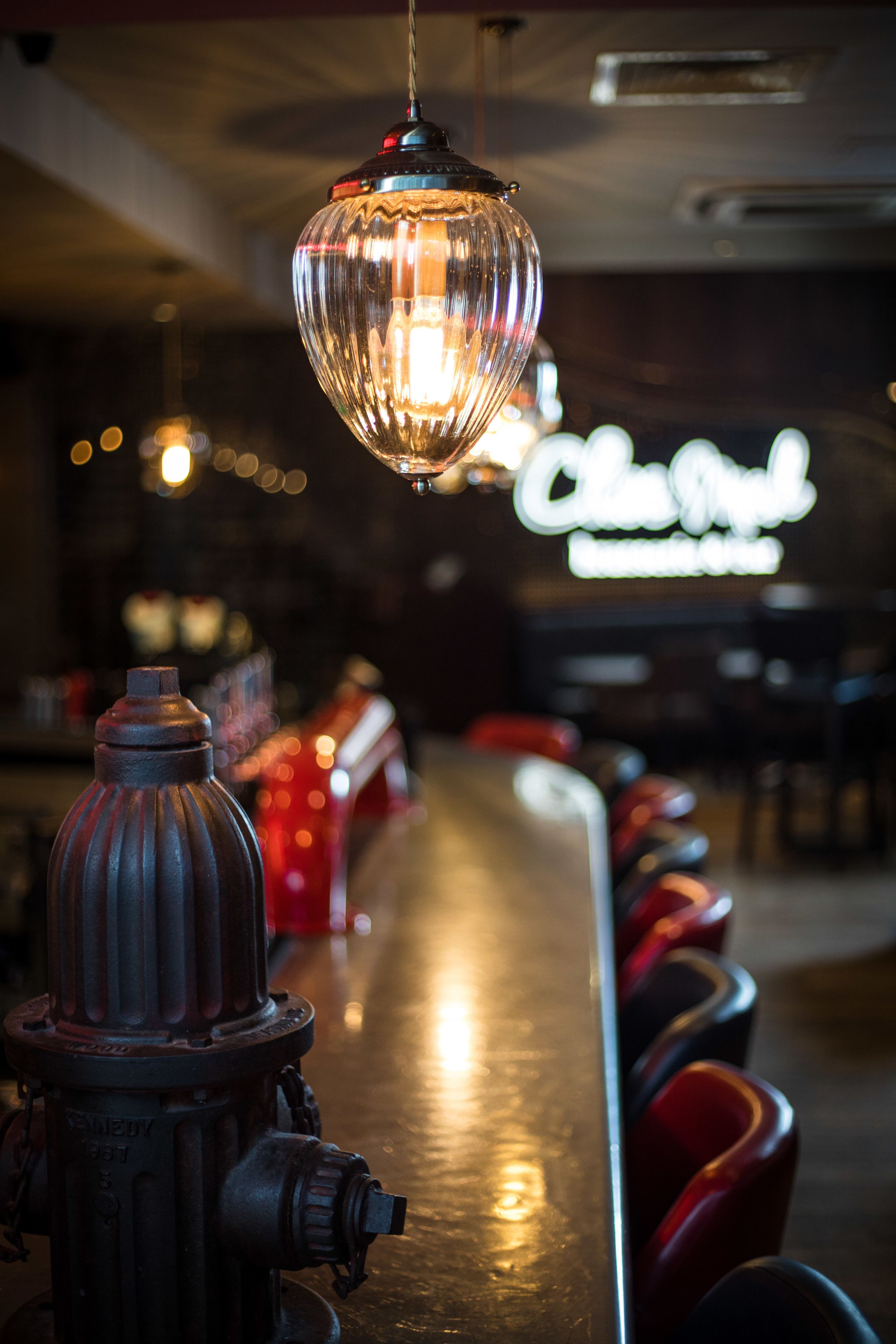 Una zona de bar con un hidrante, una lámpara colgante y un letrero de neón al fondo.