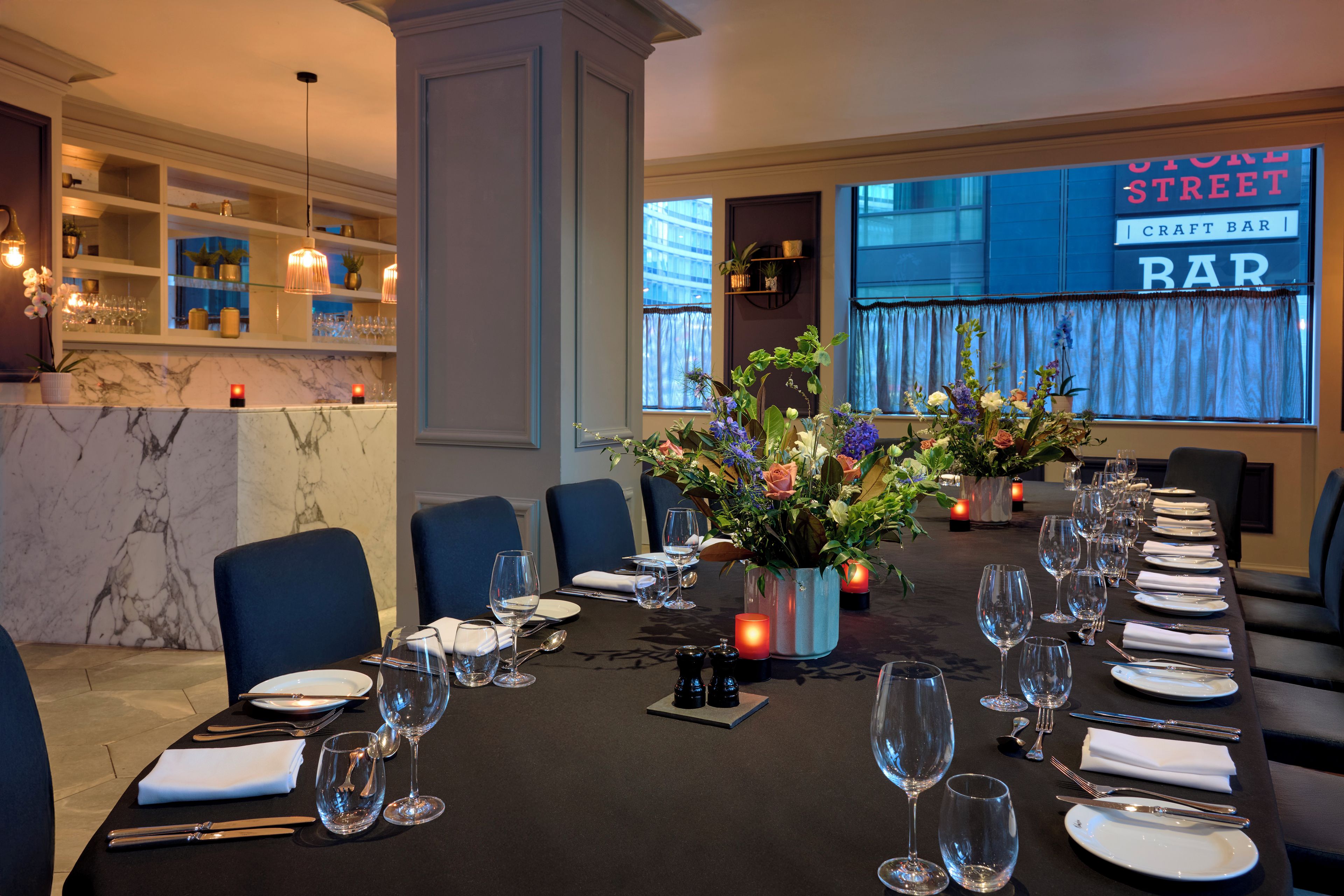 Une salle à manger élégante, avec une longue table dressée pour un repas, des chaises et un centre de table décoratif.
