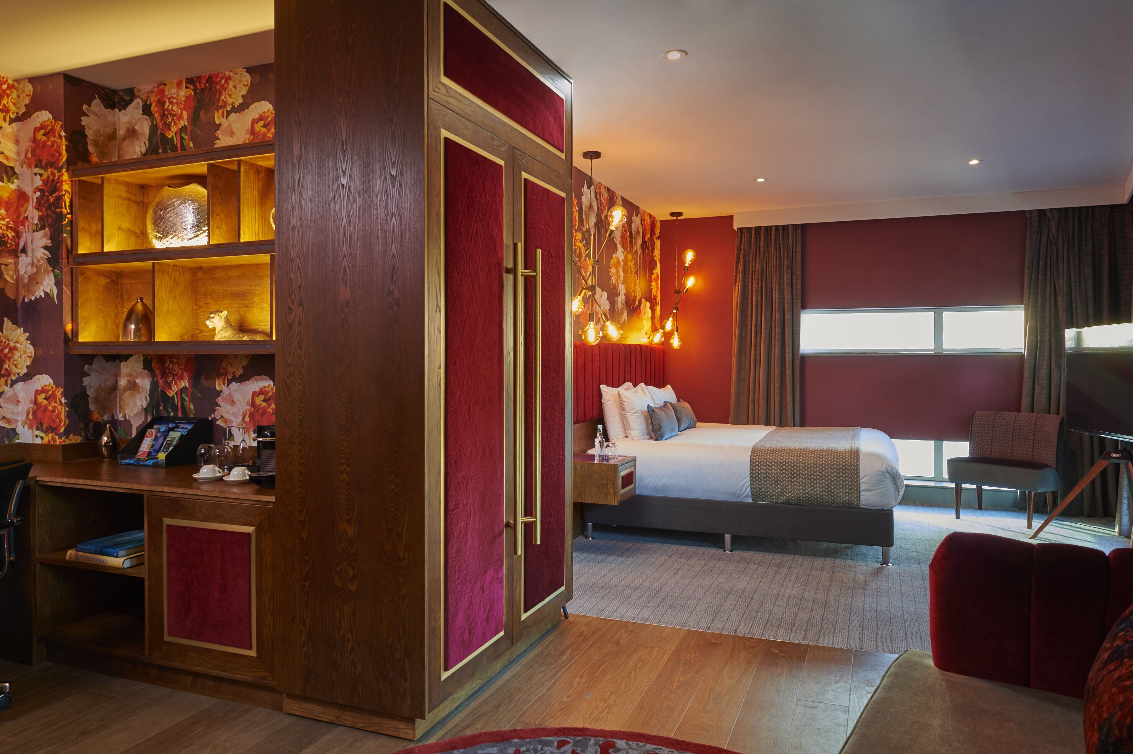 A hotel room with a bed, a desk, a bookshelf, and a large window.