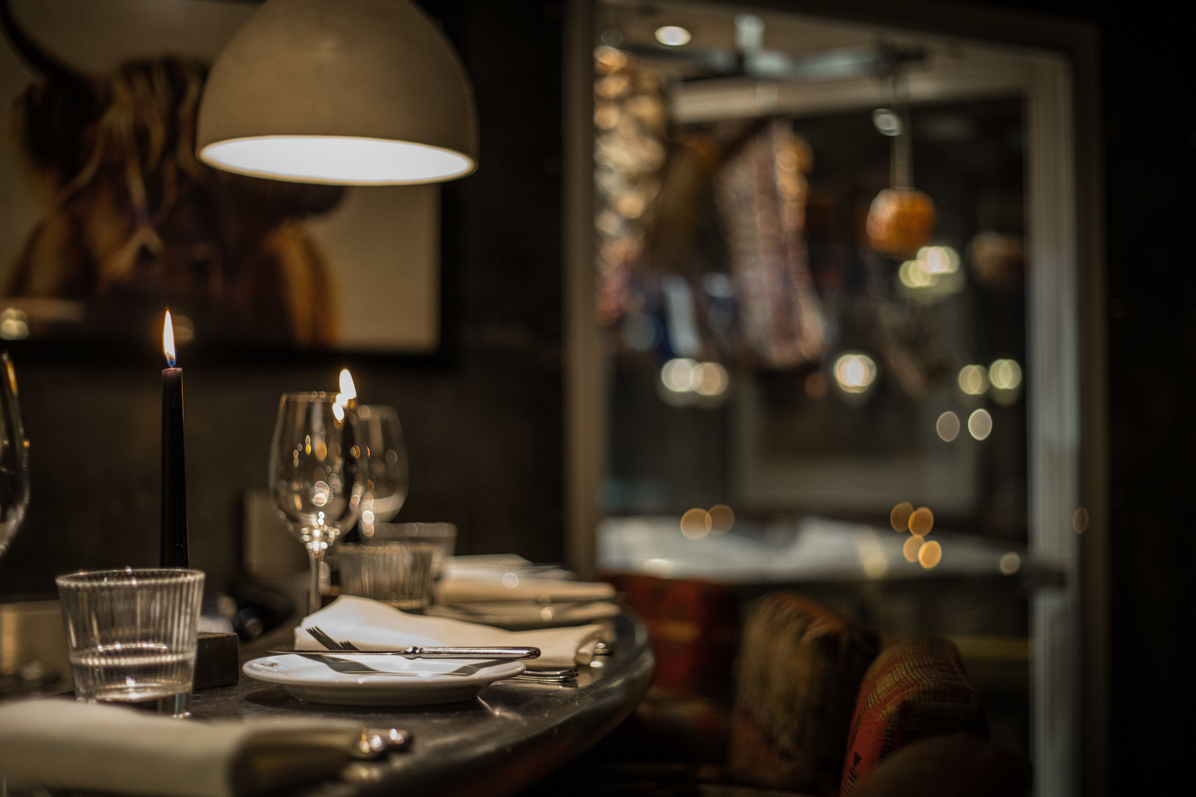 A dimly lit restaurant interior with a candle on the table, glasses, and a window view of a cityscape.