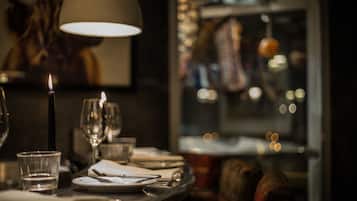 A dimly lit restaurant interior with a candle on the table, glasses, and a window view of a cityscape.