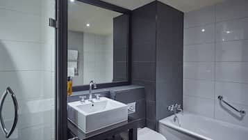 A modern bathroom with a large mirror, a white sink, a bathtub, and a toilet.