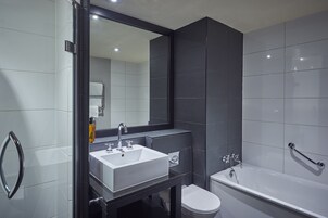 A modern bathroom with a large mirror, a white sink, a bathtub, and a toilet.