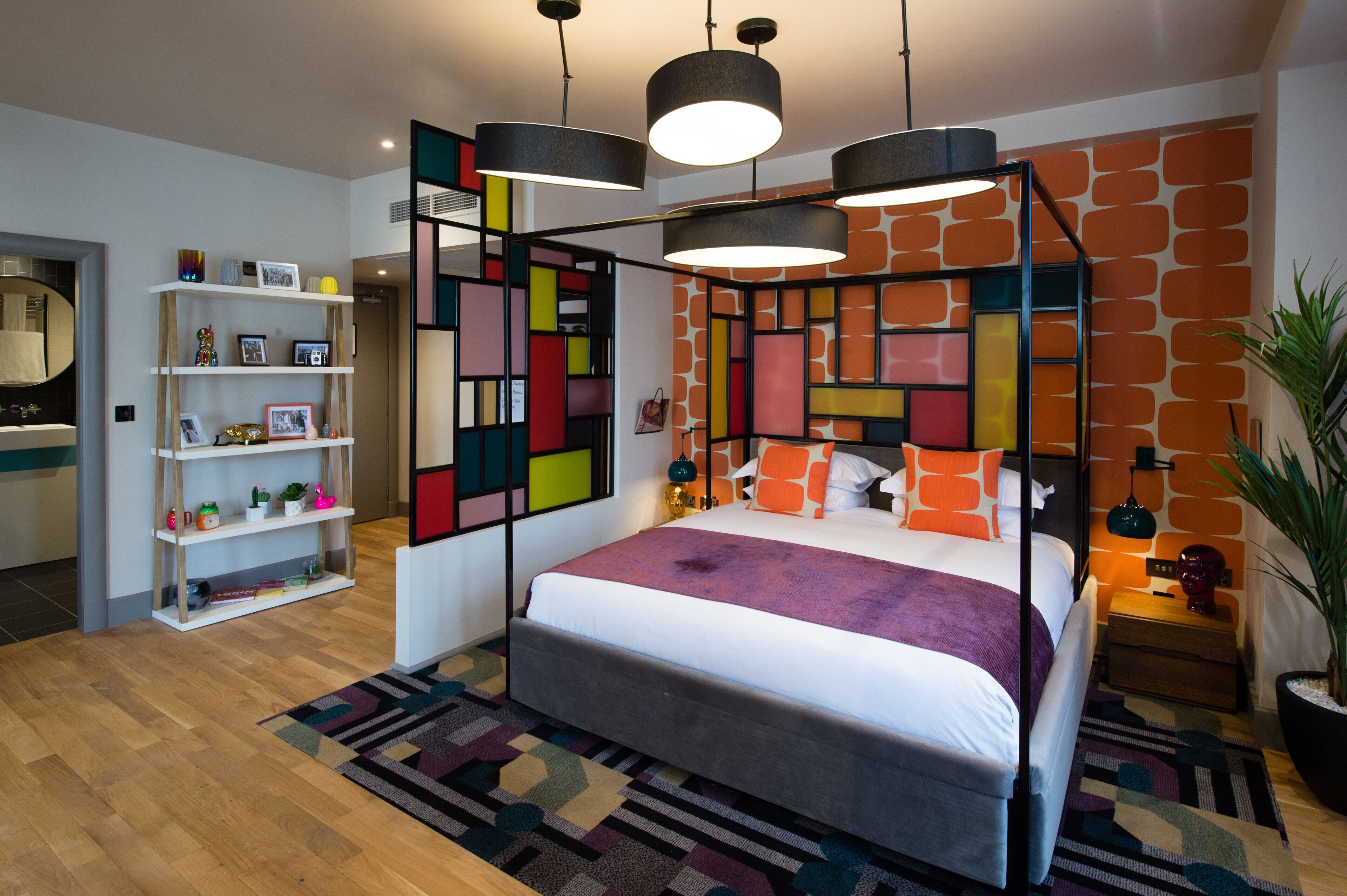 Un dormitorio moderno con cama con dosel, una estantería y una pared con estampado geométrico.