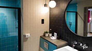 A modern bathroom with a blue and white tiled wall, a round mirror, a sink, and a shower area.