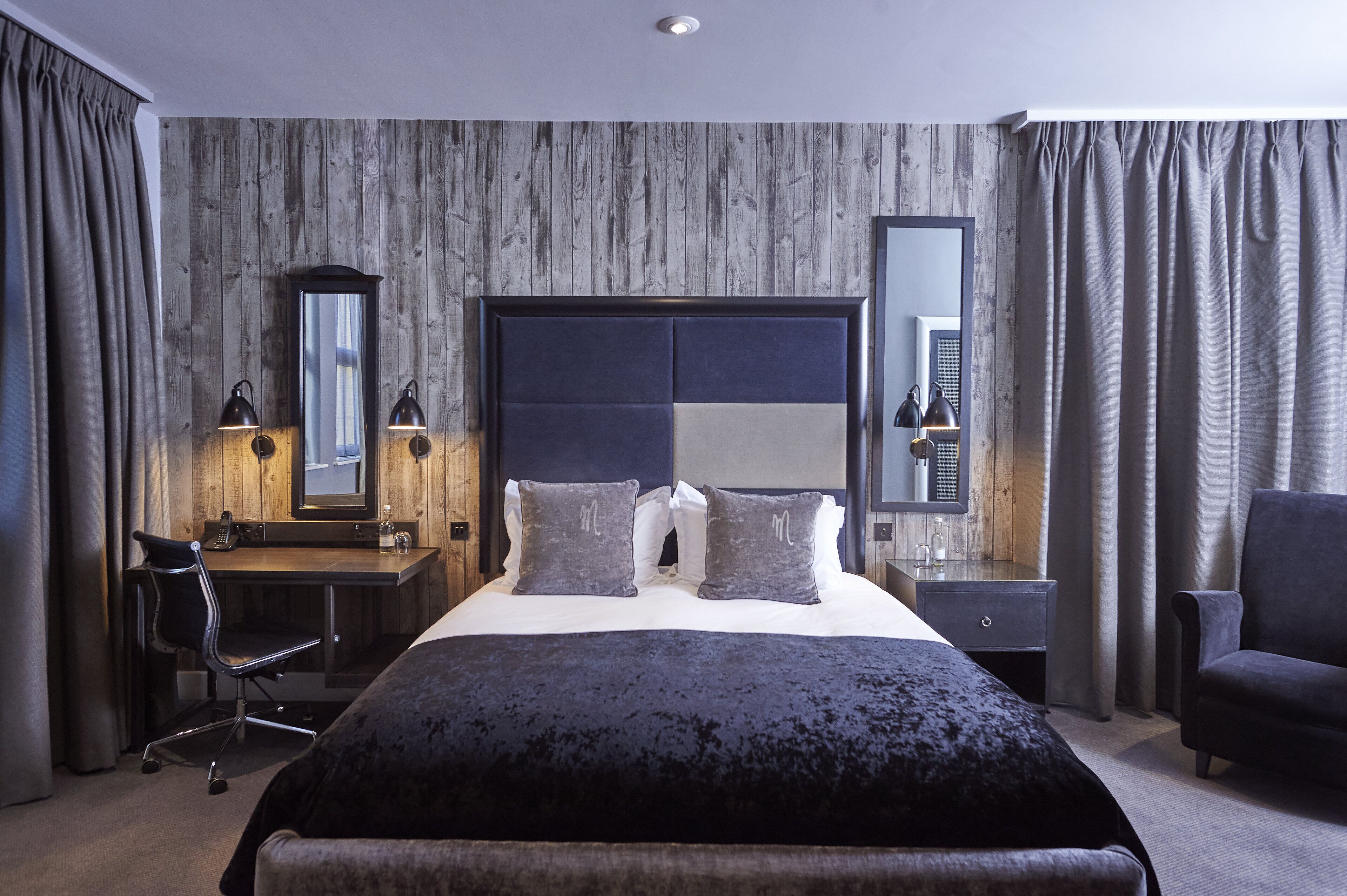 A modern hotel room with a large bed, a desk, and a chair.