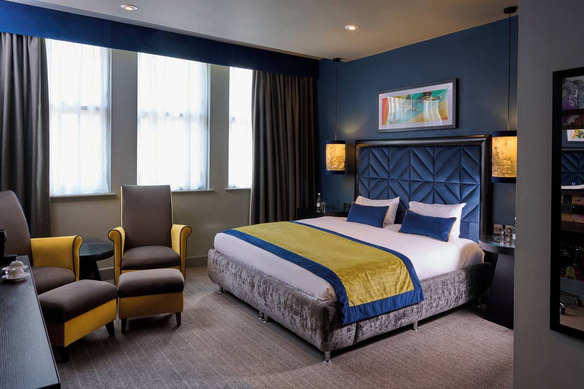 Une chambre d’hôtel avec un grand lit, deux fauteuils, une petite table et une bibliothèque.