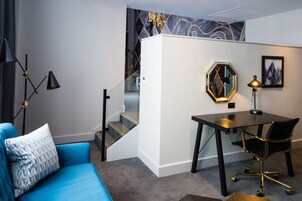 Una habitación moderna con un sofá azul, un escritorio con una silla, una escalera y una pared con patrones geométricos.