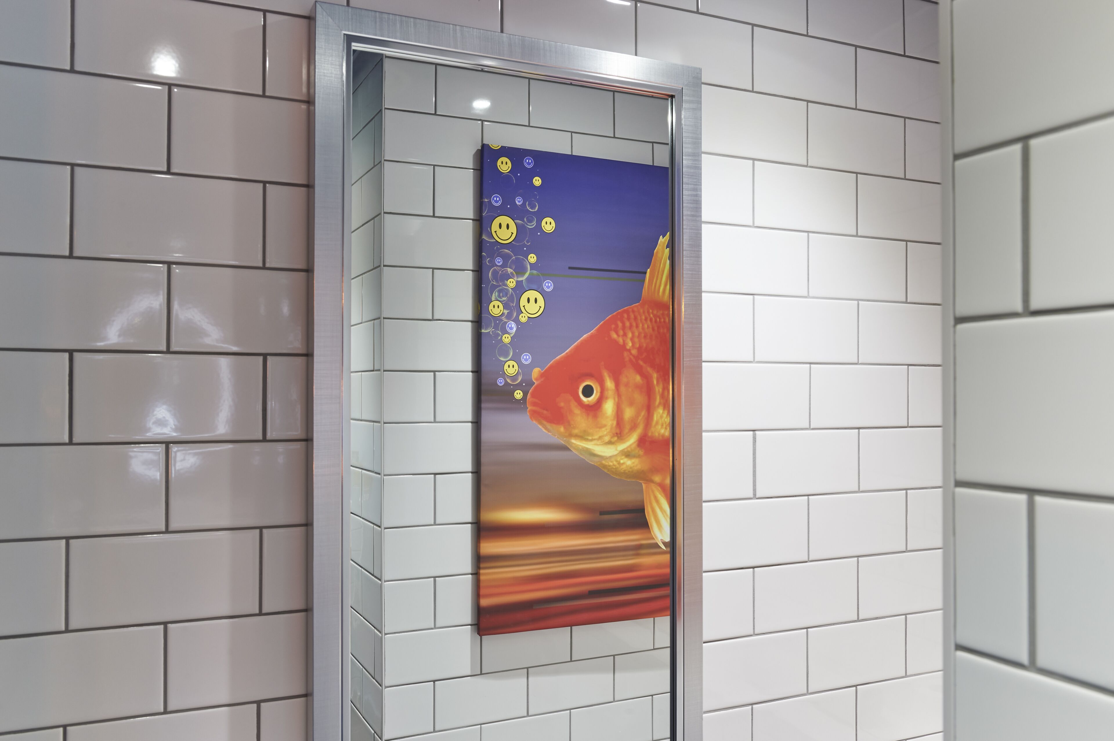 A framed artwork of a goldfish with bubbles on a white tiled wall.