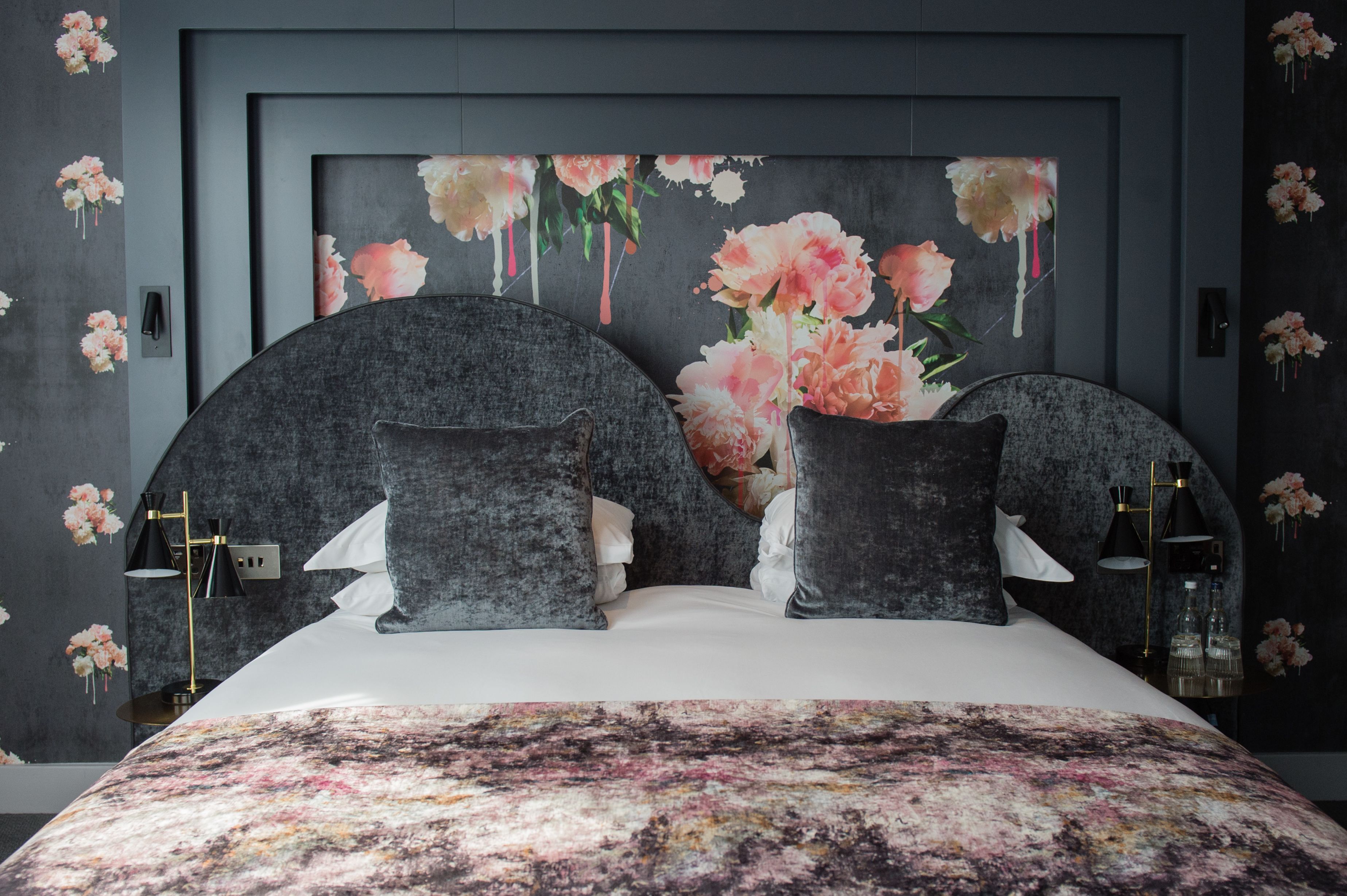 Un dormitorio con una cama grande, cabecera oscura y papel tapiz con motivos florales.