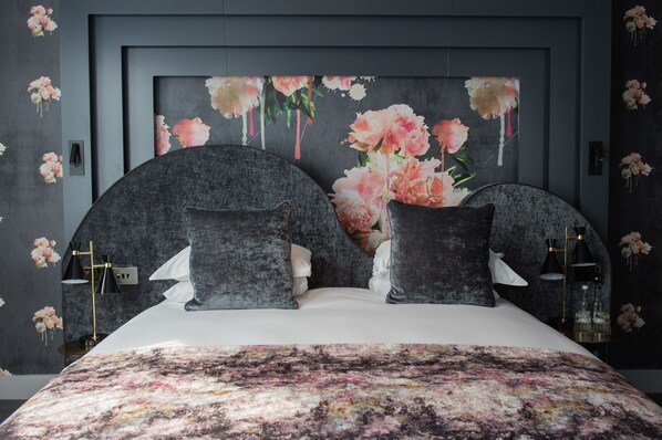 A bedroom with a large bed, dark headboard, and floral wallpaper.