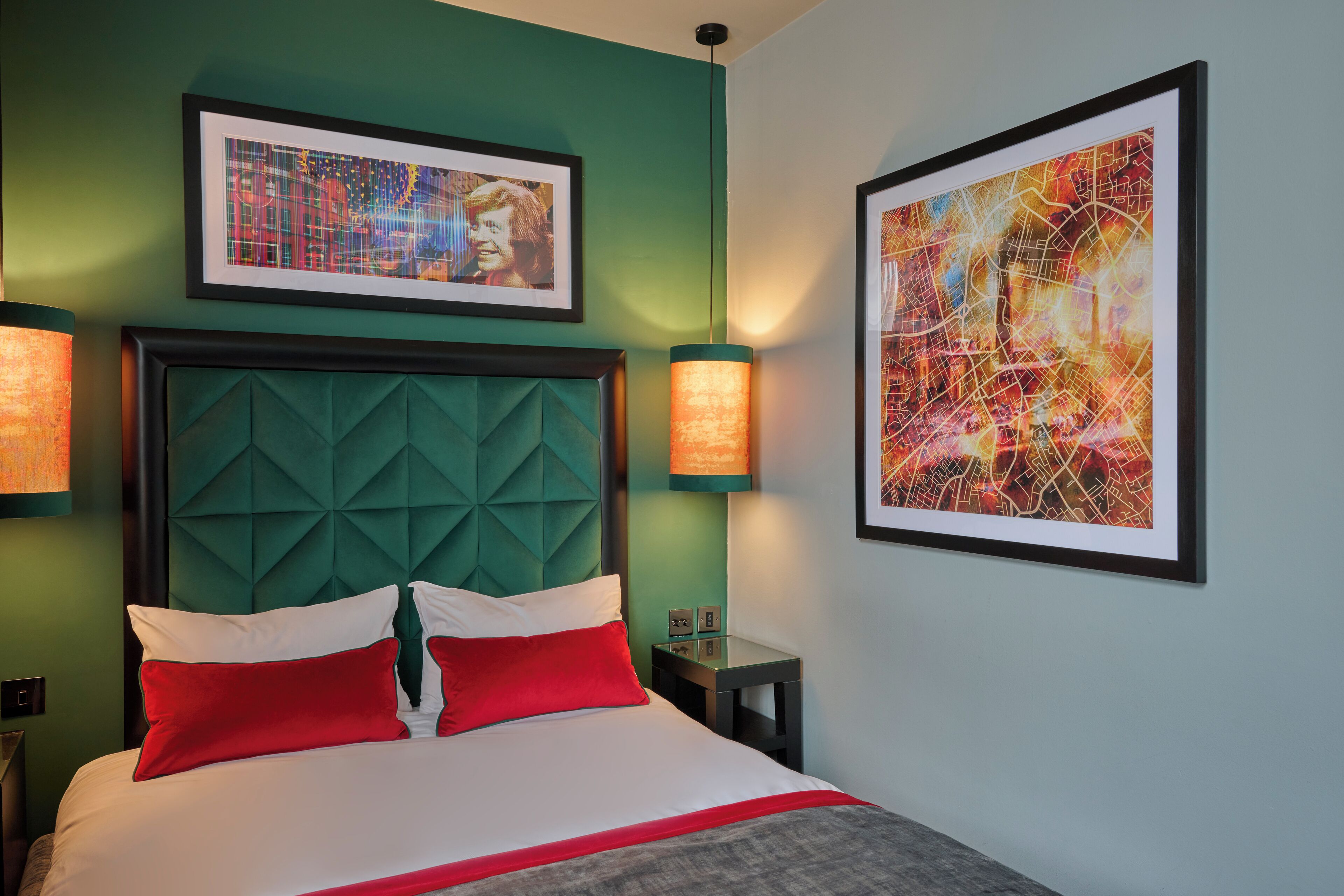 A modern hotel room with a large bed, green accent walls, and two framed artworks above the bed.