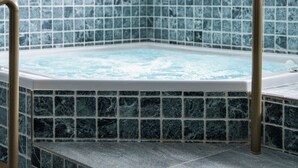 A hot tub with a tiled floor and steps leading up to it, surrounded by a white tiled wall.