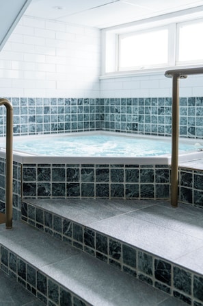 Un jacuzzi con piso de baldosas y escalones que llevan a él, rodeado por un muro de azulejos blancos.