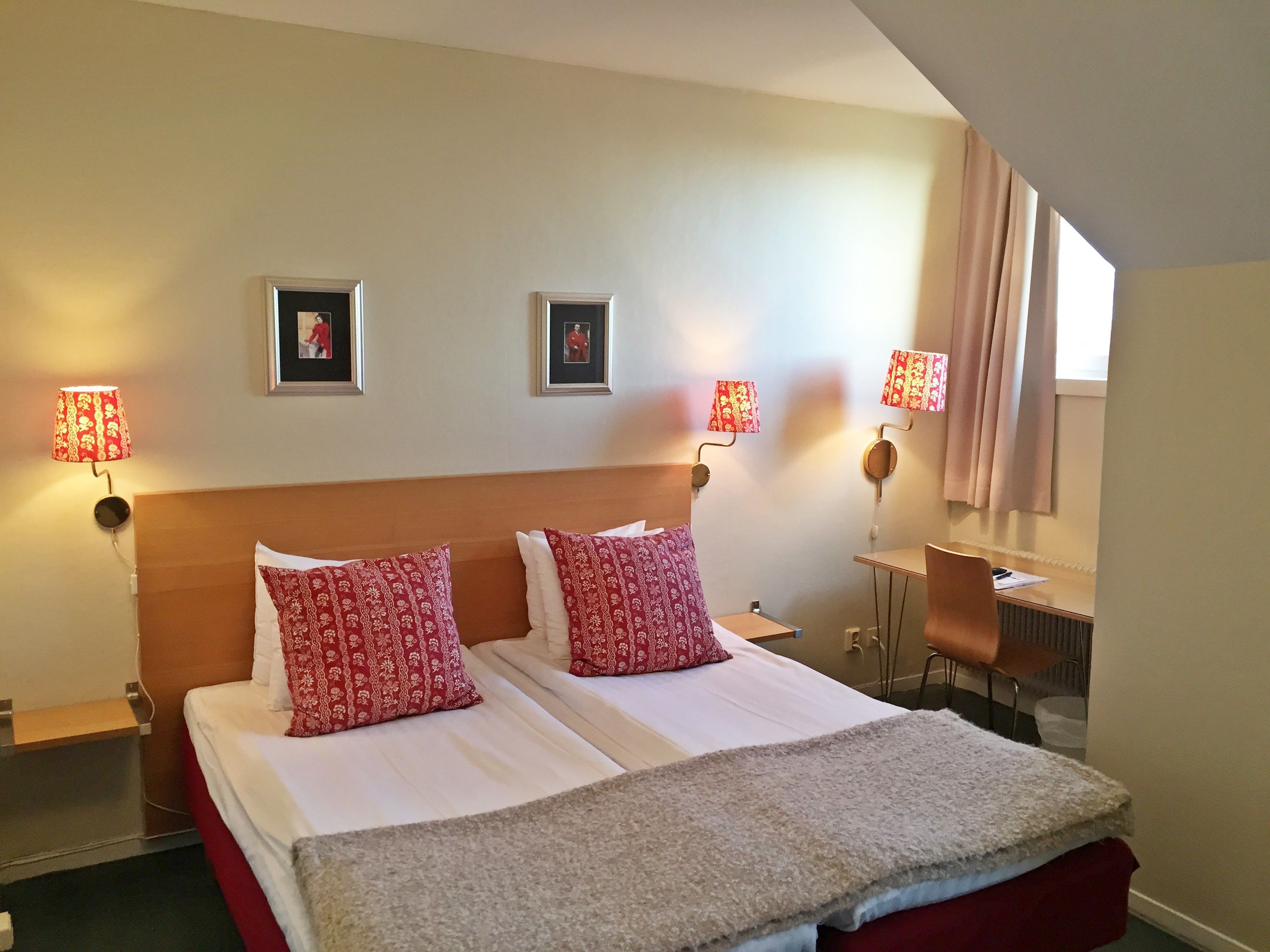 Ett hotellrum med en säng, två sänglampor, ett skrivbord och en stol.