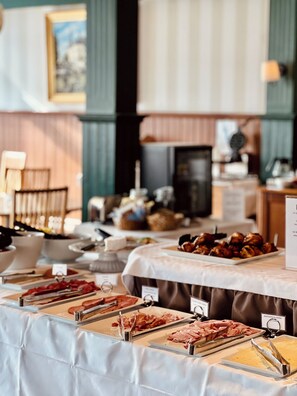 A buffet with various food items and utensils, a sign indicating a price, and a background with a framed picture and a fireplace.