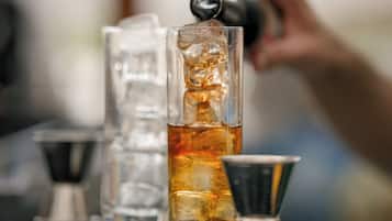 A bar setting with a tall glass filled with a golden liquid, ice cubes, and a metal jigger.