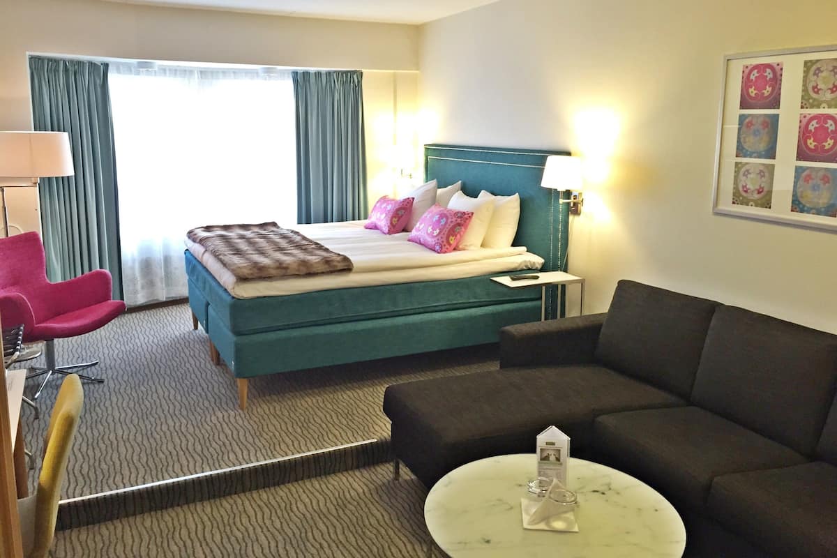 Une chambre d’hôtel avec un lit, une chaise, un canapé, une petite table et une lampe.