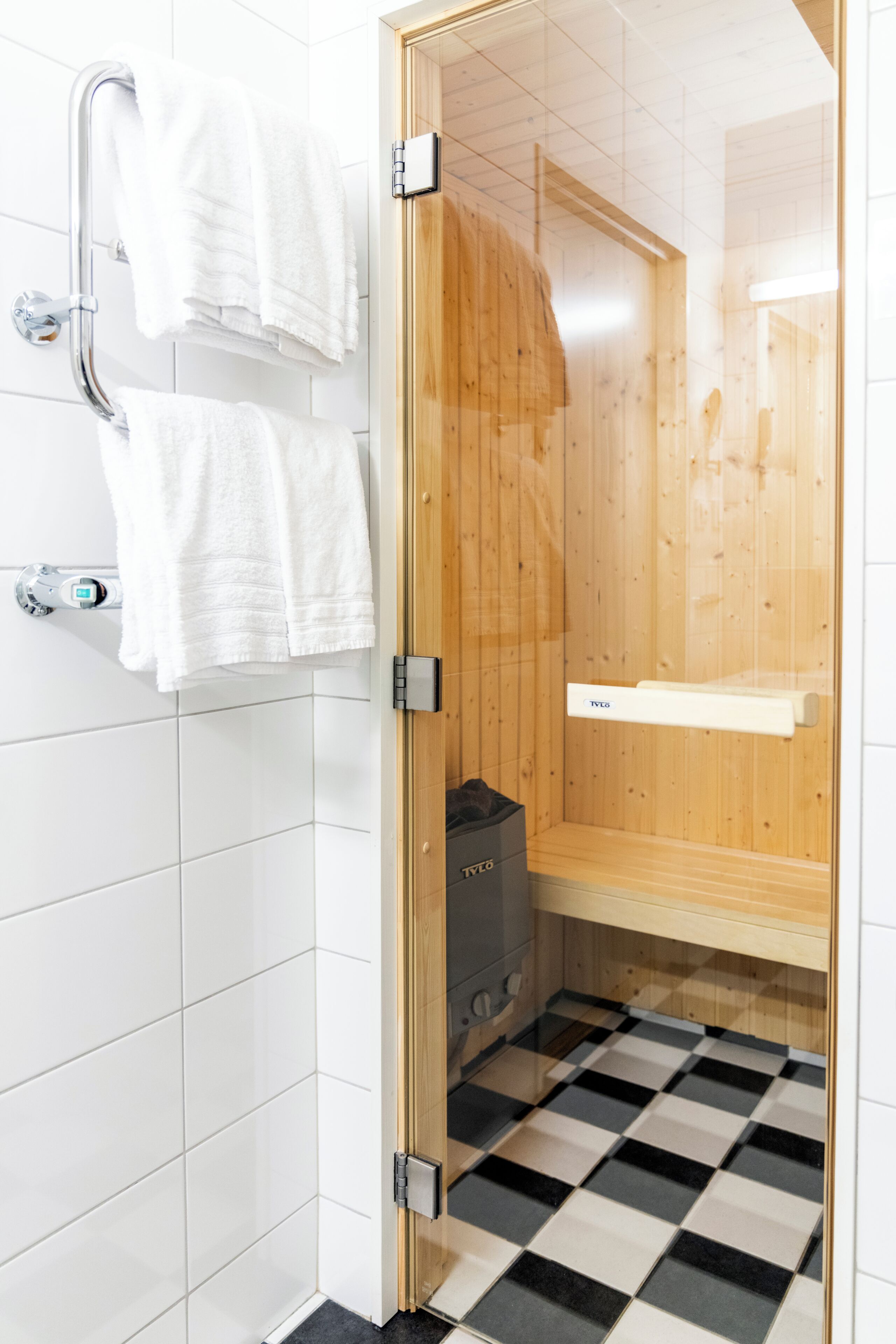 Eine Dusche mit Holztür, weißen Fliesenwänden und einem Schachbrettfußboden.