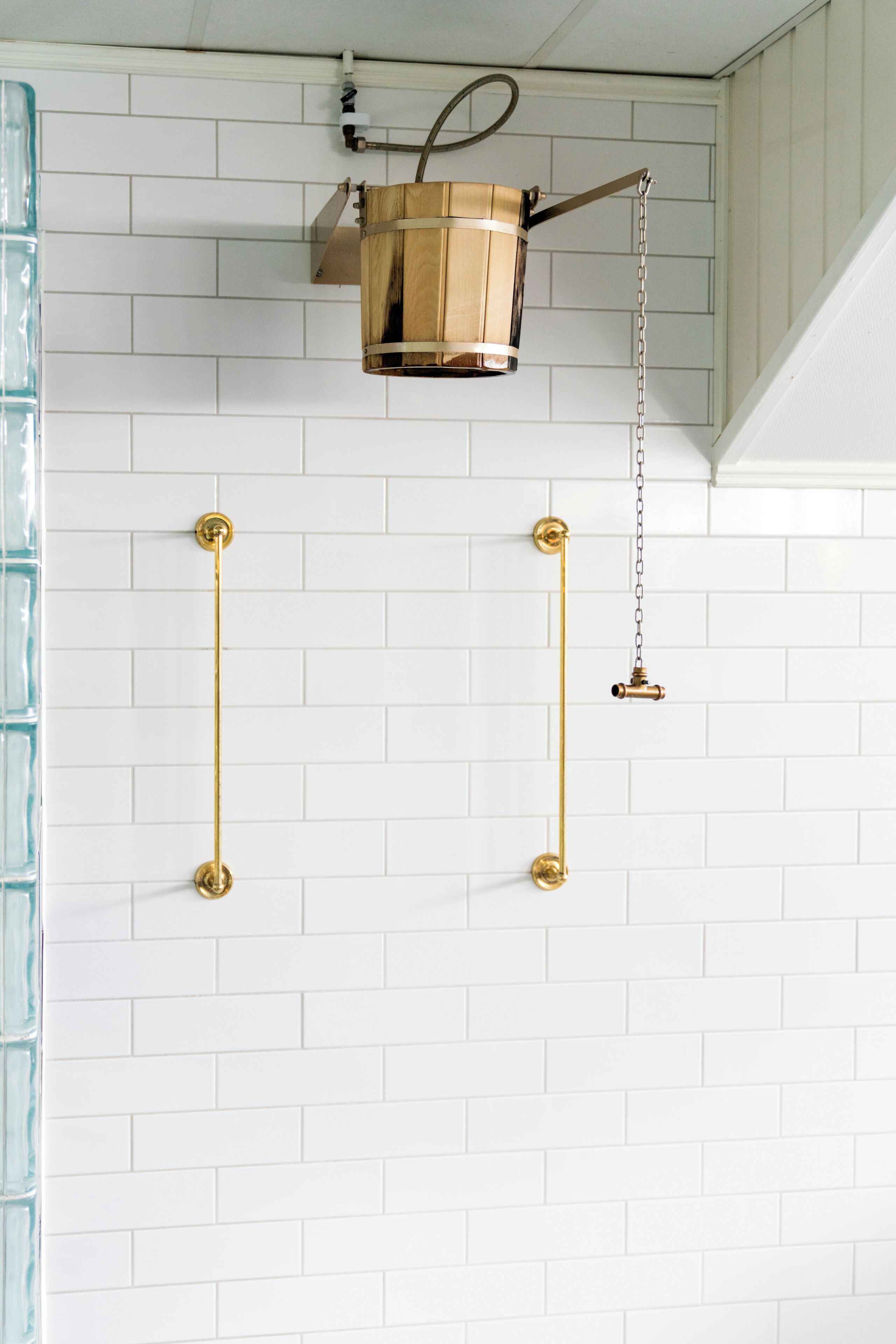 A bathroom with white tiled walls, a wooden bucket fixture, and brass fixtures.