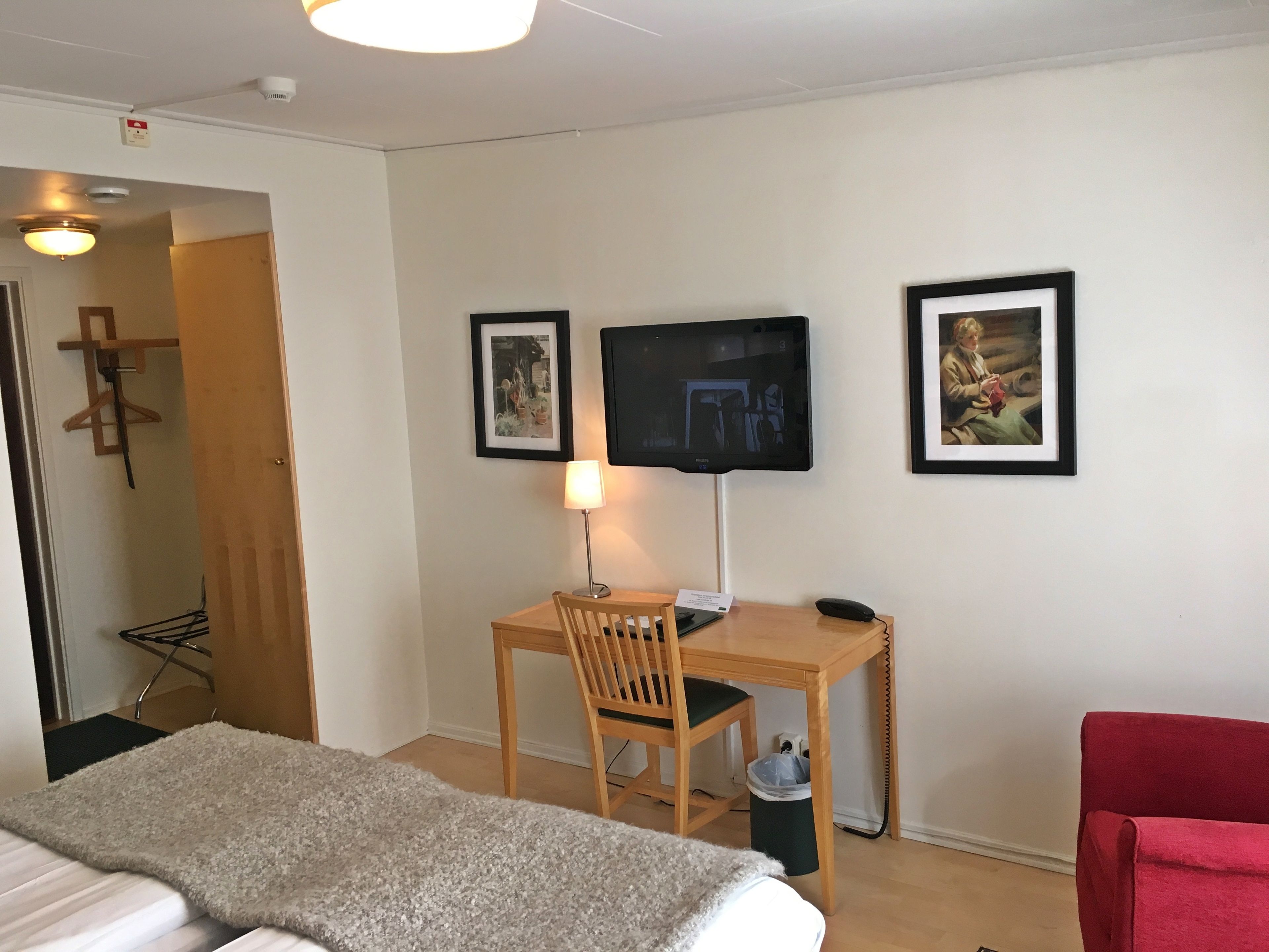 Une chambre d’hôtel avec un lit, un bureau équipé d’un ordinateur, une télévision et deux tableaux encadrés au mur.