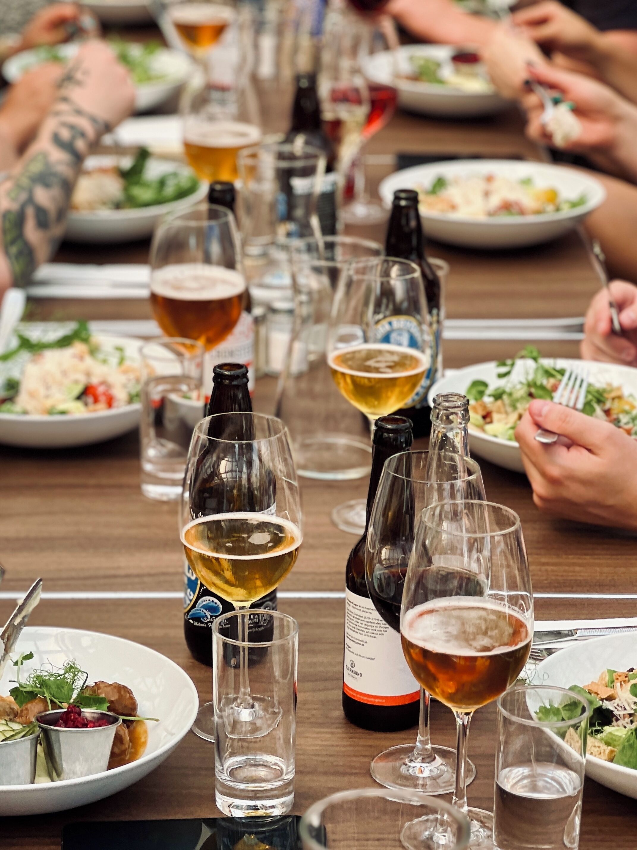 A dining table with multiple glasses of beer and bottles, surrounded by people.